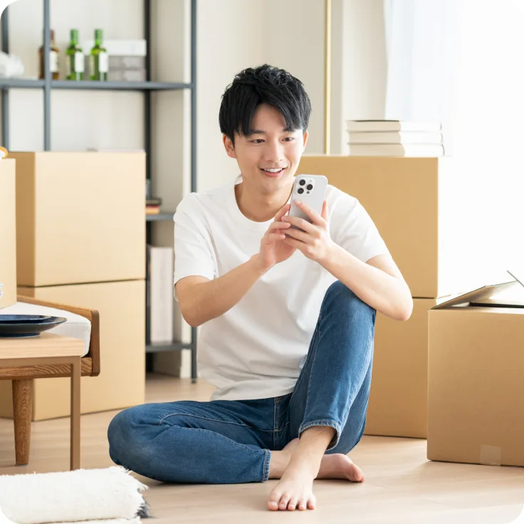 段ボールに囲まれた部屋でスマートフォンを操作する男性